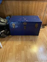 Front angle view of blue metal chest showing wear and two metal latches on the front.