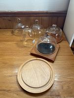Five glass cloche domes arranged behind two wooden cheese boards on wooden surface
