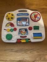Full view of the Fisher Price 1993 vintage crib toy white plastic activity board with multiple colorful interactive elements including a yellow wheel, red knob, reflecting mirror and blue roller.