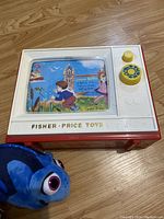Top front view of the Fisher Price Music Box TV and a Dory plush toy on wooden floor.
