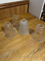Four glass lamp shades on a wood table, showing their shape and general condition
