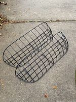 Two large black wire wall garden/planter baskets shown on pavement, visually good condition, curved design, grid wire construction.