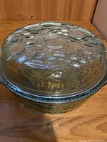 Top view of green glass casserole dish with pie plate lid, showing embossed textured fruit design on lid surface.