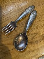 Pair of vintage children's silver plated spoon and fork with embossed Mickey Mouse handles placed on a wooden surface.
