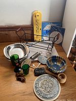 Photo showing assortment of kitchenware, decorative bowls, glassware, wooden figurines, and other miscellaneous household items all arranged on a surface.