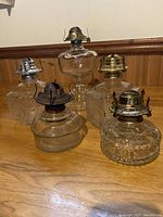 Front view of five vintage clear glass oil lamp bases with metal wick holders on a wooden surface.