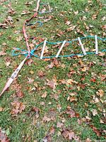 Photo showing the rope ladder with wooden rungs and blue ropes laid out on grass with fallen leaves.