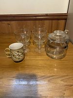 Photo showing all items together on a wooden surface: Pyrex coffee pot with lid, vintage mug, and four clear pedestal goblets.