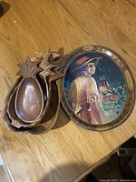 All items displayed together on wooden floor. Four wooden bowls nested and one Coca-Cola metal serving tray beside them.