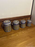 Set of 4 blue and yellow ceramic canisters in descending size order on wooden surface against wall.