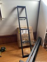 Black rectangular assembled wall shelf frame leaning against the wall showing open shelving slots.