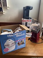 Photo showing all three appliances: the black Starfrit coffee maker on its box, the Nostalgia Electrics popcorn popper, and the boxed Hamilton Beach Sorbetiere ice cream maker open on the table.