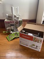Shot of Starfrit spiralizer, 5 blades displayed in front, crank handle visible, box included.