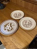 Three vintage dinner plates arranged on a wooden surface showing their floral designs and condition.