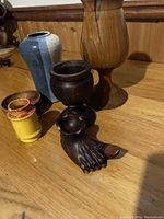Photo of all six items arranged on wood surface: two tall wood vases, blue/white pottery vase, yellow bud vase, wood bowl and wood foot incense/ashtray.