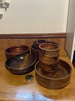 Lot of 10 assorted wooden bowls with various sizes and depths placed on a wood surface against a wall.