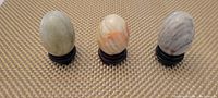 Top front view of three marble and onyx eggs on dark round pedestals showing different stone colorations.