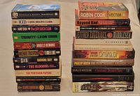 Photo showing two stacks of various paperback and hardcover books by bestselling authors, titles visible on spines.