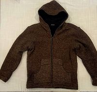 Front view of brown woolen jacket with hood, metal zipper, and two large front pockets laid flat on a light surface.