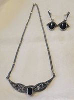 Photo showing the full necklace with delicate double chain and the pair of drop earrings with black onyx set in geometric sterling silver frames accented with marcasite stones.