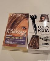 Front view of the L'Oreal Perfect Blondissima Crème Blonde streaking highlight kit alongside L'Oreal Colorista Bleach Decolourant highlights kit box, both displaying product branding and hair model images.