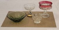 Four vintage colored glass dishes and bowls arranged on a mat, showing pink, green, and clear pressed and cut glass pieces.
