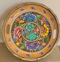 Top view of the round wooden tray showing the brightly painted floral design with a wavy edge and dark gold-painted rim with built-in handles.