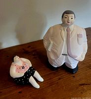 Both ceramic figurines displayed together on a wooden surface, showing scale and relative size of man and woman figurines.