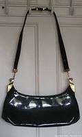 Front view of the black patent leather purse with brass hardware, showing adjustable strap.