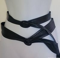 Two black leather fashion belts modeled on a mannequin to show style and fit; skinny belts crossed on waist with black oval and round buckles.