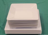 Stack of 6 larger white square melamine plates shown atop a stack of 16 smaller plates, all are smooth and glossy white.