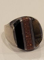 Front view of the sterling silver men's ring showing the black and reddish glittery stone inlay design.