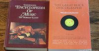 Two music reference books: 'The Golden Encyclopedia of Music' hardcover and 'The Great Rock Discography' paperback placed side by side on a wooden surface.