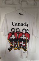Front view of the white T-shirt with Canada hockey players graphic and 'Canada' text above.