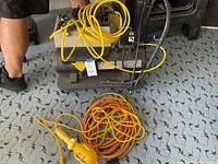 Overview showing air compressor, orange extension cord, and yellow shop light all placed on patterned floor.