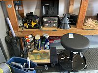 Photo showing a black shop stool with caster wheels, automotive fluids including K&N filters and Absorbine bottle, spray cleaner, and plastic funnels on the shelving.