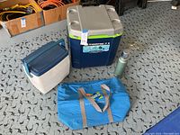 Lot contents on garage floor including coolers, insulated bag and thermos