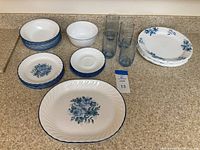Photo shows entire set arranged on countertop including the various plates, bowls, saucers, and four blue drinking glasses.