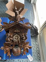 Front view showing large cuckoo clock with carved deer head, crossed rifles, squirrels, and leaf details.