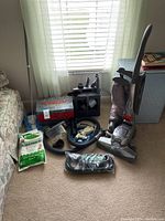 Kirby carpet shampoo system vacuum with attachments, hose, cleaning supplies, and accessories laid out on floor next to couch and cabinet.