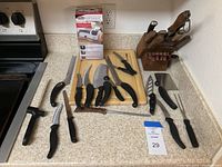 Photo of assortment of kitchen cutlery including knives, sharpener, sharpening steel, cutting board, and knife block on kitchen counter.