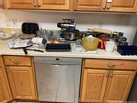 Full counter view of baking lot including electric mixer, mixing bowls, muffin tins, brownie pan, measuring cups, rolling pin, and various utensils.