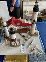 Top view showing four lighthouses positioned on table with wind chime to the side, one lighthouse with red roof attachment and cords visible