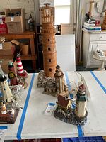 Overview photo of multiple lighthouse figurines on table in garage with boxes and cabinets in background