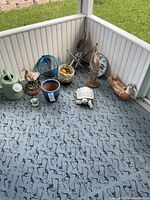 Wide view of all outdoor decor items on patio floor including watering can, pots, bird and turtle figurines, windchime, thermometer.