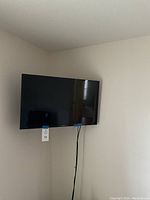 Samsung 32-inch TV mounted on beige wall showing front and side angles, cables hanging down.