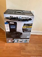 Front side of the Shark IQ Robot vacuum cleaner box showing the product image and main features like self-empty base, pet hair pickup, self-cleaning brushroll and 30 days dust collection capacity.