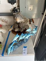 Photo showing the Six Paws gray wolf sculpture on a wooden base alongside the dolphin centerpiece with multiple blue dolphins on wave-like base.