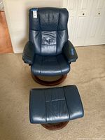 Front view of blue leather Stressless chair and matching ottoman on carpet, showing wooden bases.