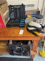Overall view showing black Husky tool bag hanging front side of wooden workbench, assorted drill bit case and several small containers on bench